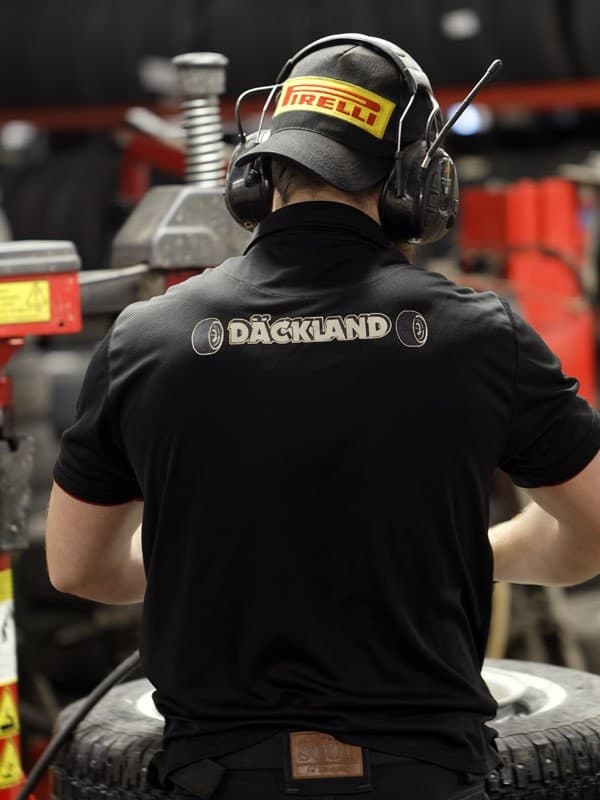Ryggen på en mekaniker i svart arbetströja med Däckland-loggan, vid däckmaskinen